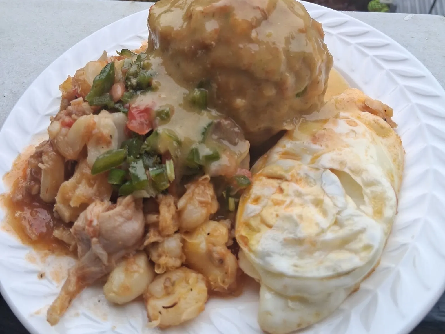 A bolón, seco de pollo with mote and chopped green peppers, and a fried egg on a white plate